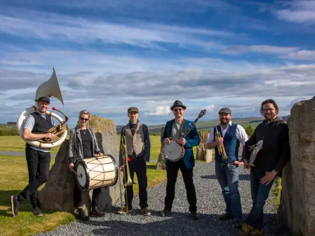 Members of a band standing together smiling holding their instruments.